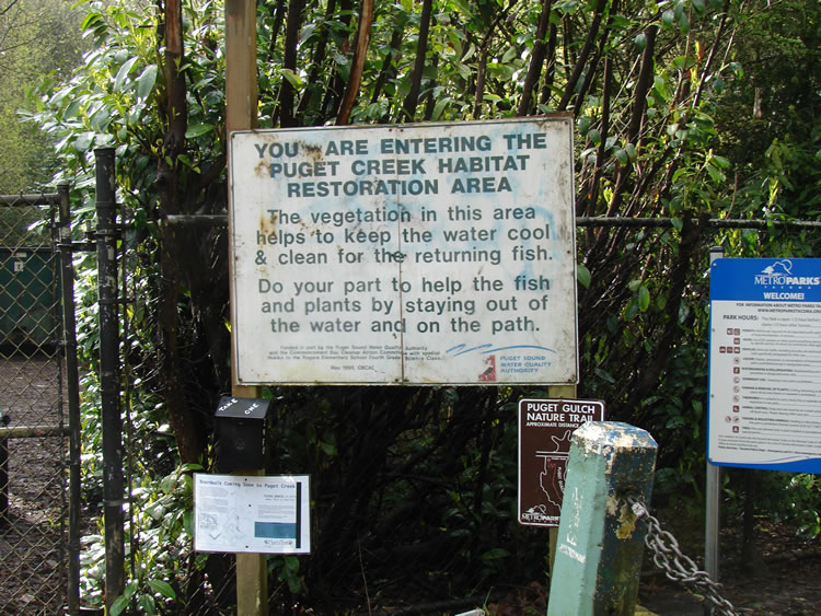 A large white sign alerting passersby to the habitat restoration area and asking them to stay on the path.