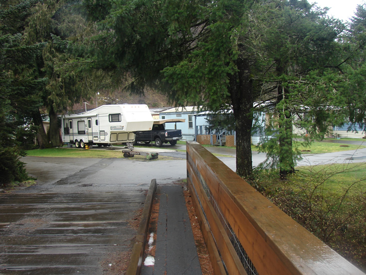 A bridge with a wooden railing on a paved road leading to some trailers