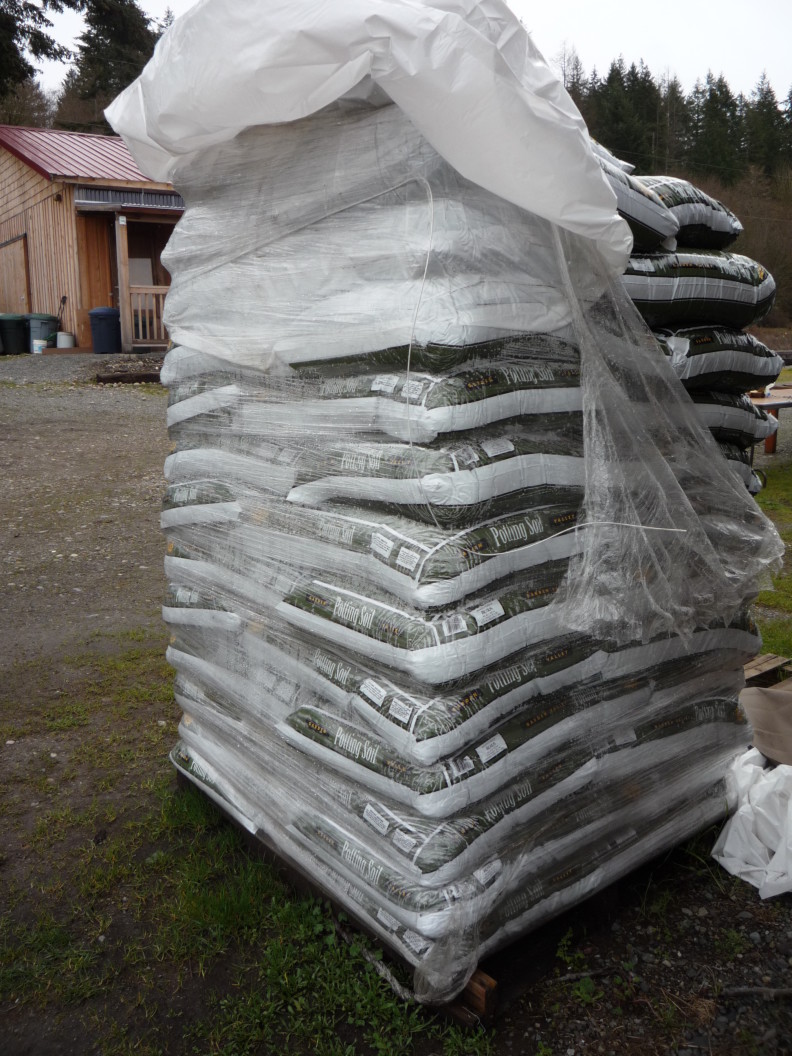 a pallet of bags of potting mix with plastic around it. the top right corner has the plastic torn off