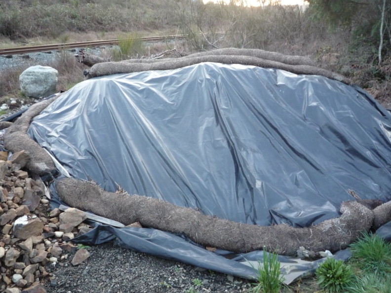 a tarp spread over something lumpy. rolls of coconut coir hold the tarp down