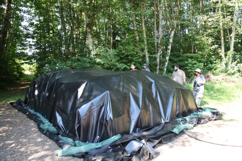 piles of pots under a large black tarp being steamed for disinfection