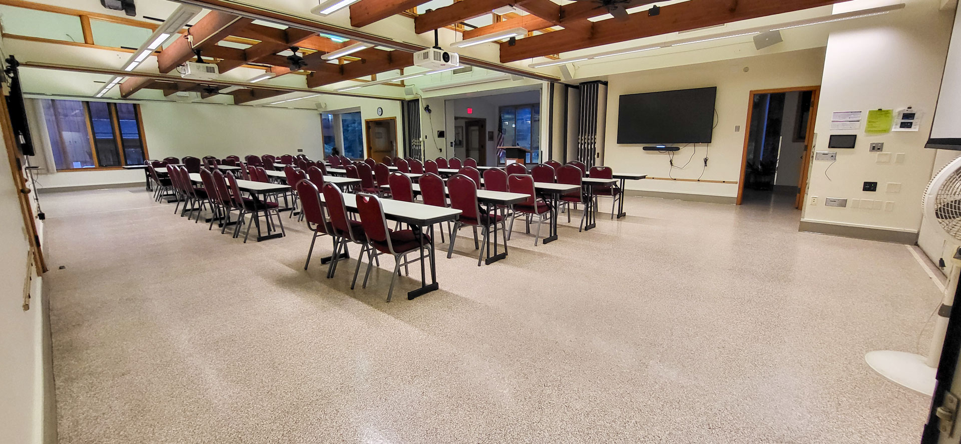 Tables and chairs in a large, open meeting room. Large monitor on the front right wall.