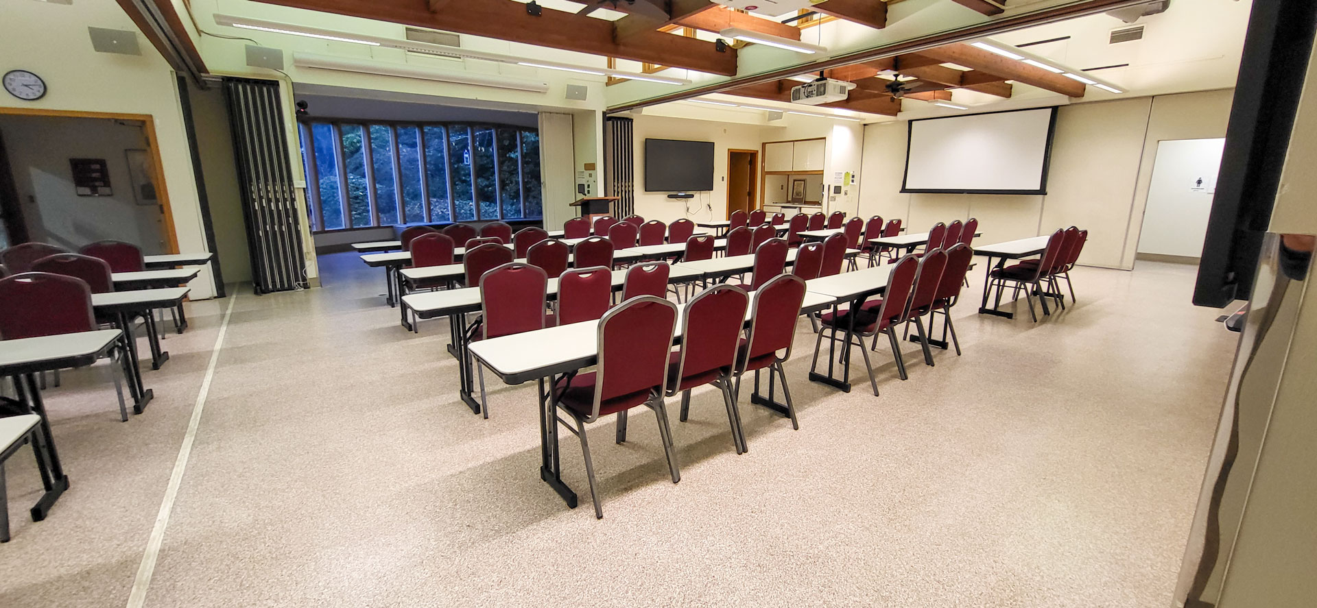 Tables and chairs face a podium and building lobby in a large meeting room.