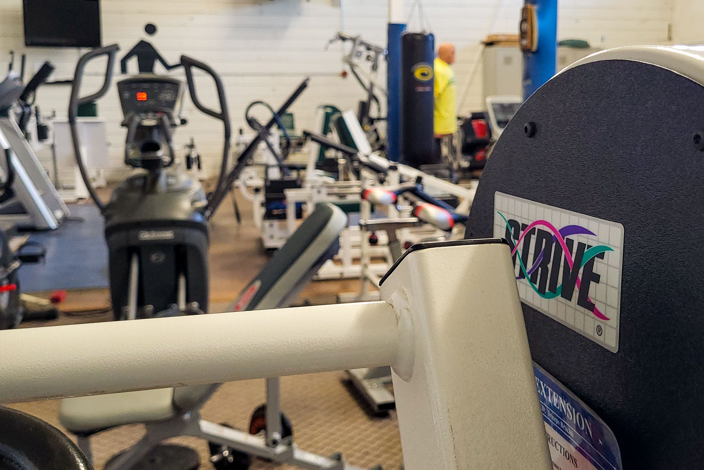 Detail of an exercise machine; other equipment in background.