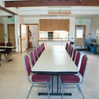 Two eight foot tables arranged end to end for meetings. Kitchen in the background.