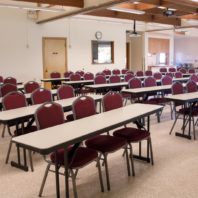 Narrow tables arranged in ranks for presentation. Kitchen and projection room in the background.