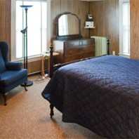 Small bedroom with single bed, chair and dresser.