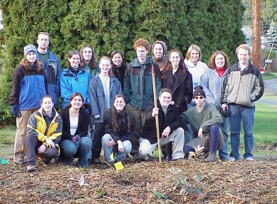 Group photo, two rows. Main in center front holds a rake.