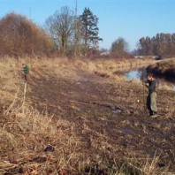 Two men install piezometers beside waterway.