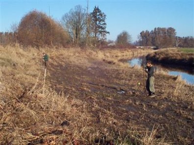 Two men install piezometers beside waterway.
