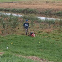 Man mowing grass plot next to waterway.