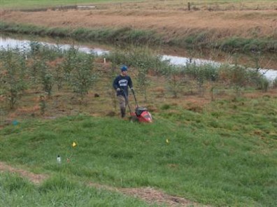 Man mowing grass plot next to waterway.