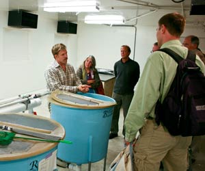 John Stark stands behind a large blue holding tank and addresses visitors
