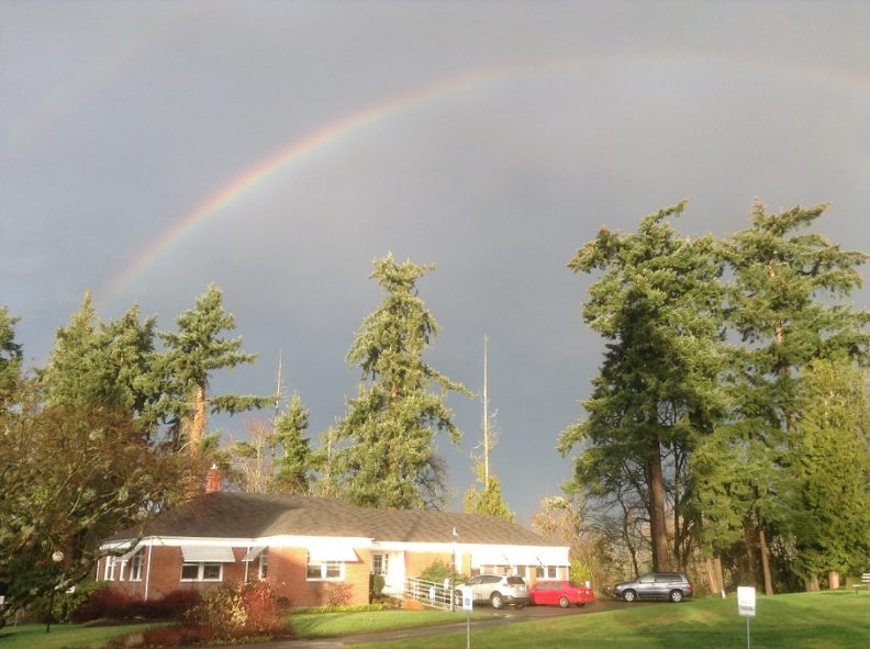 Rainbow against a gray sky over a brick building.