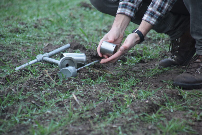 Researcher demonstrating soil bulk density sampling technique