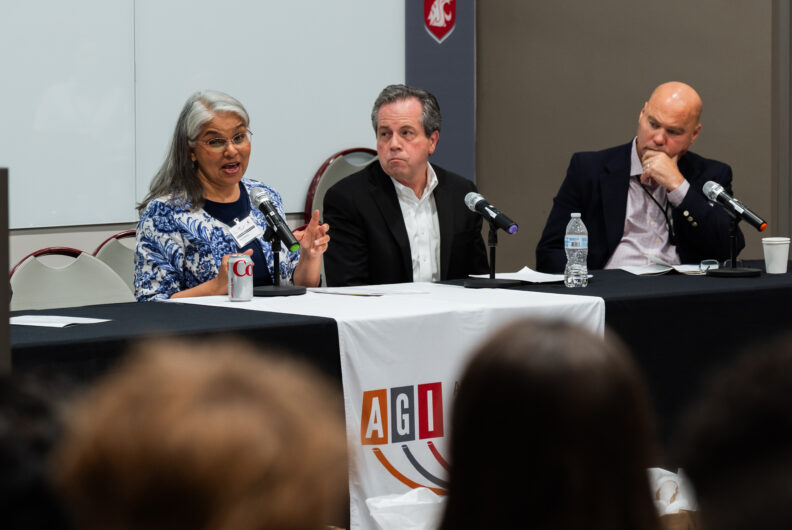 Three people on a panel, woman speaking into a microphone