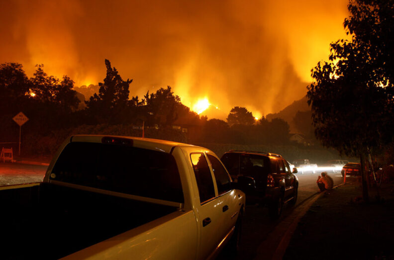 Residents of a neighborhood watch from their cars as a fire threaten their homes.