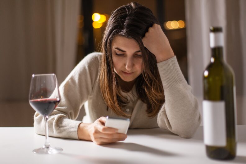 Woman using a phone with a wine glass nearby