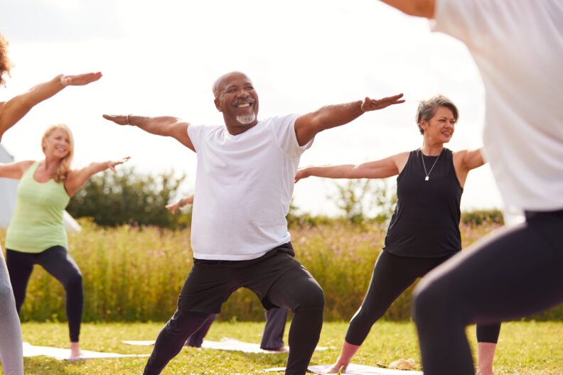People doing yoga outdoors, focused on one man in particular.