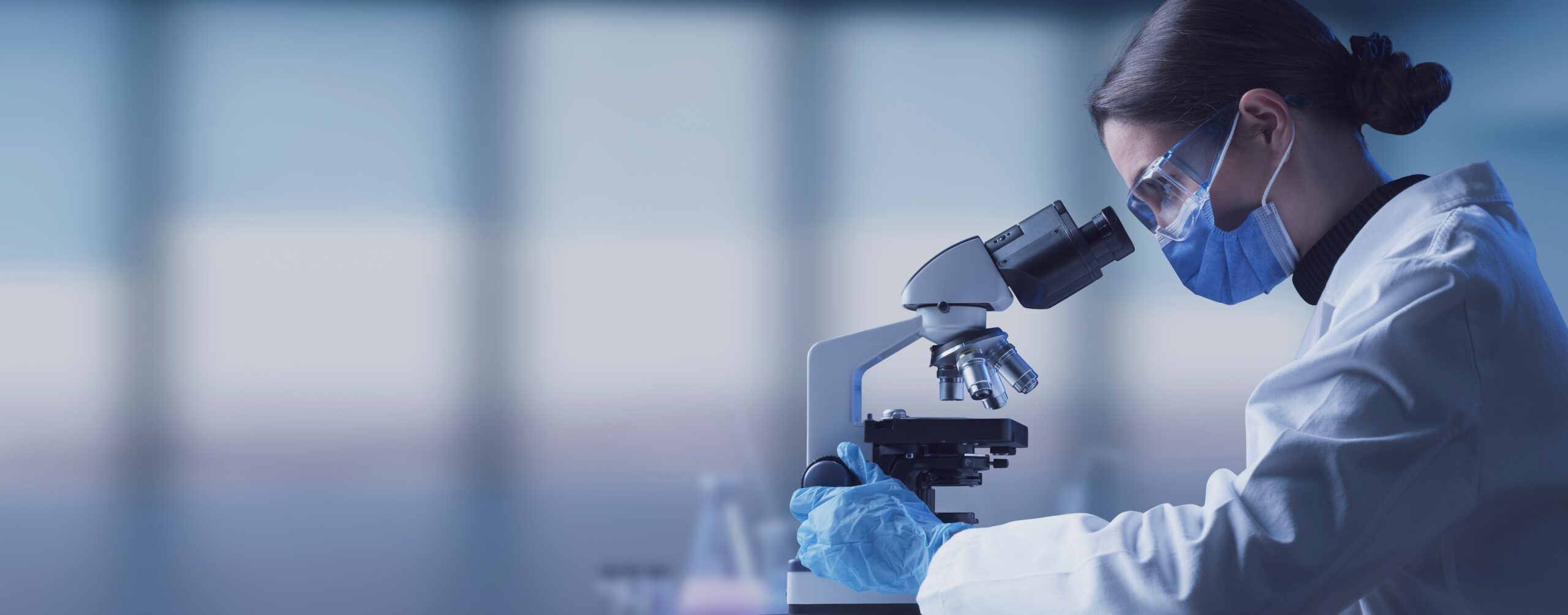 Researcher wearing a surgical mask and looking through a microscope