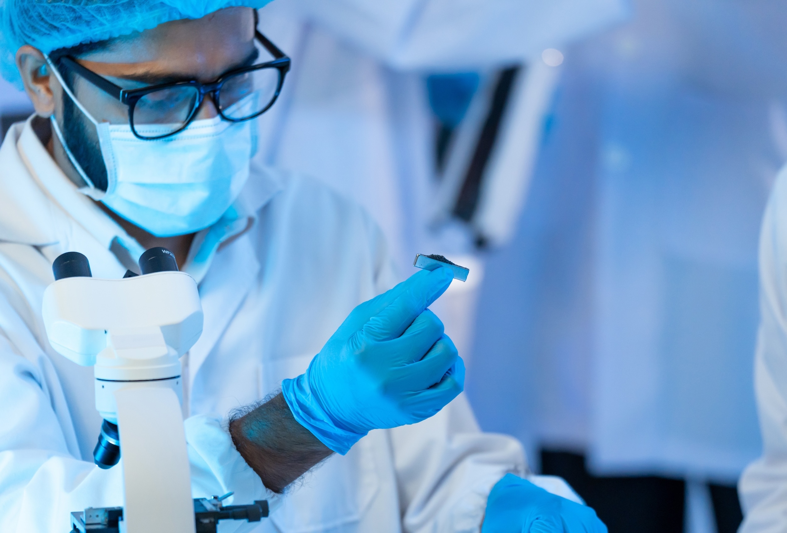 Researcher in mask, glasses and blue gloves examining small specimen