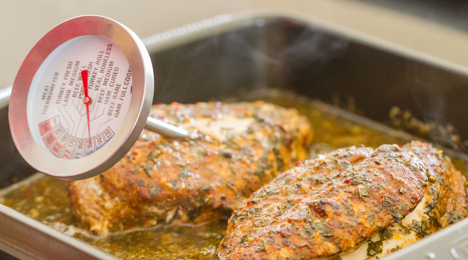 Two pieces of chicken in a baking dish, one with a meat thermometer.