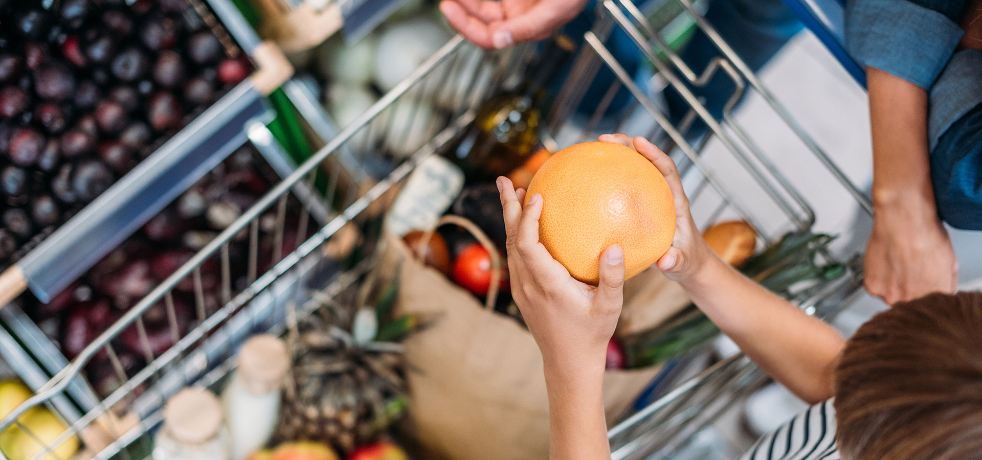 A child holding a grapefruit over a grocery cart.