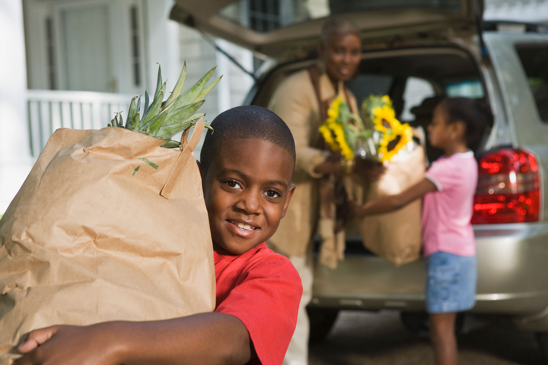 Son carrying groceries with mother and daughter near the car with more groceries.