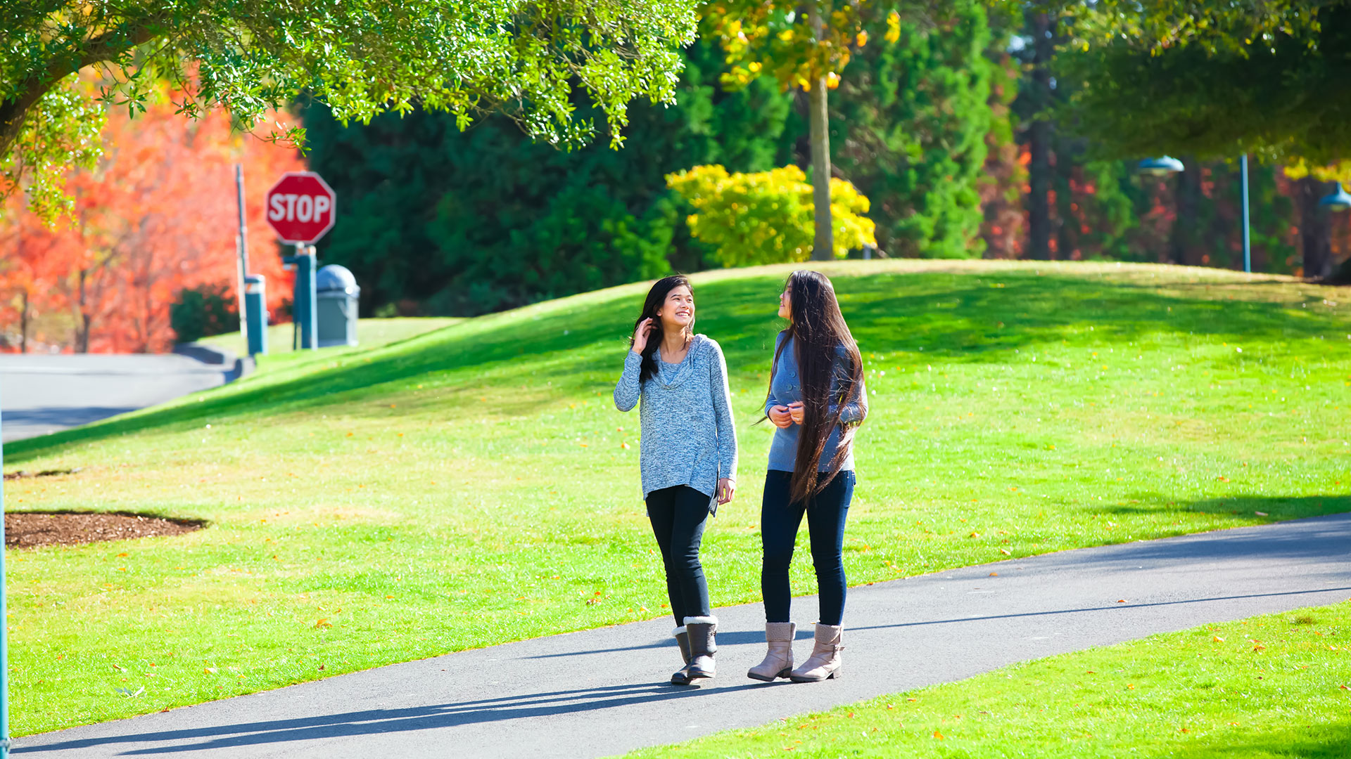 Two girlfriends walking on a path in a park on a sunny day.