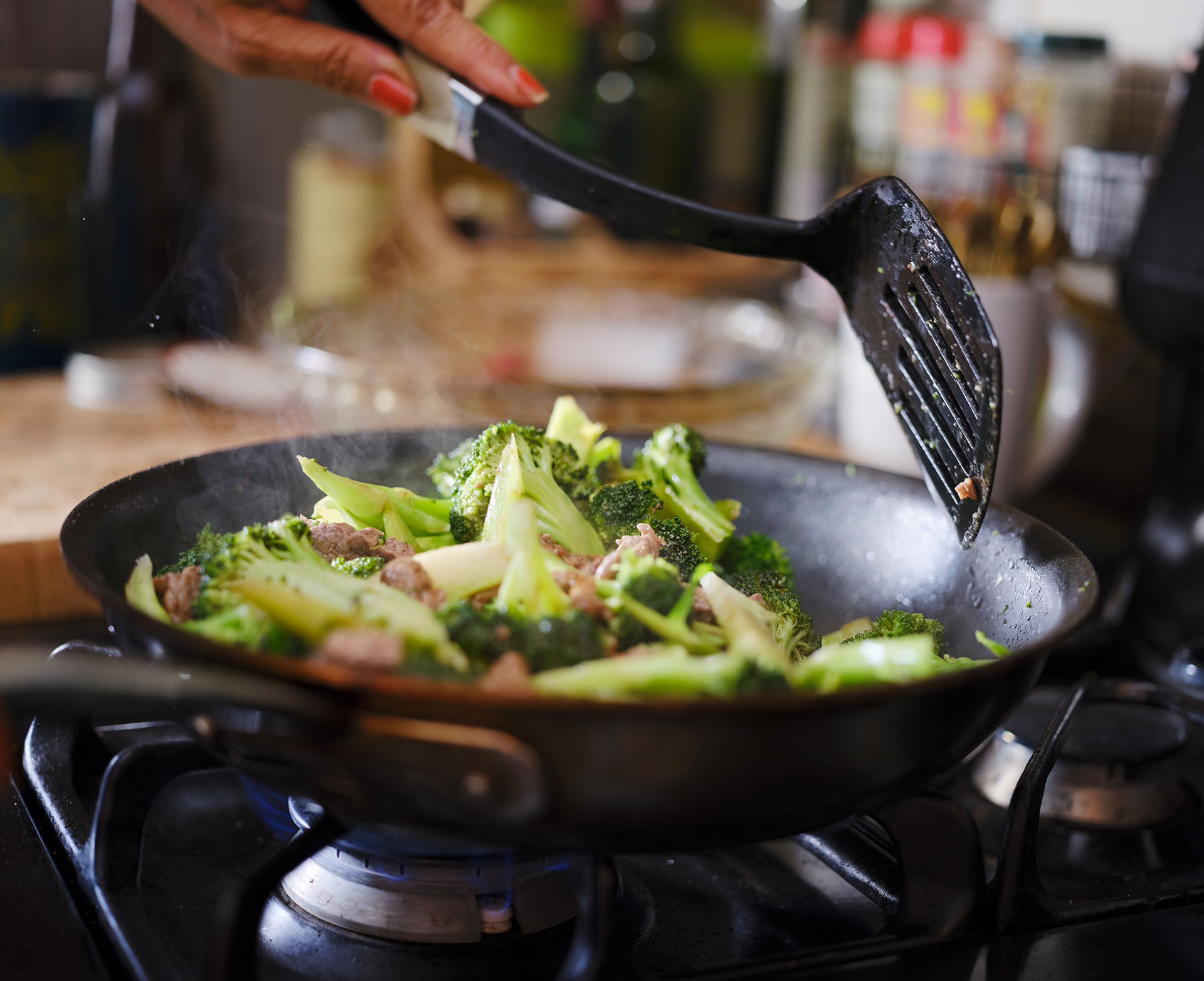 A skillet with beef and broccoli on a gas stove.