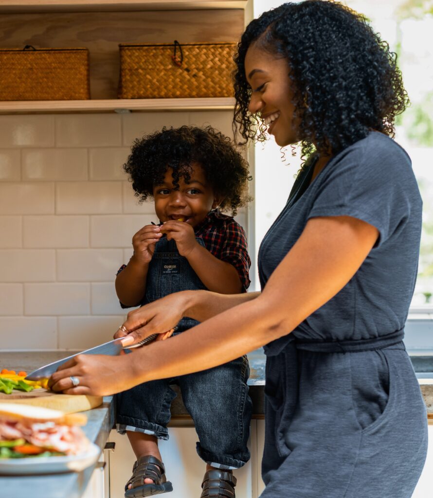 Woman cutting up sandwich with a youth sitting on the counter next to her.