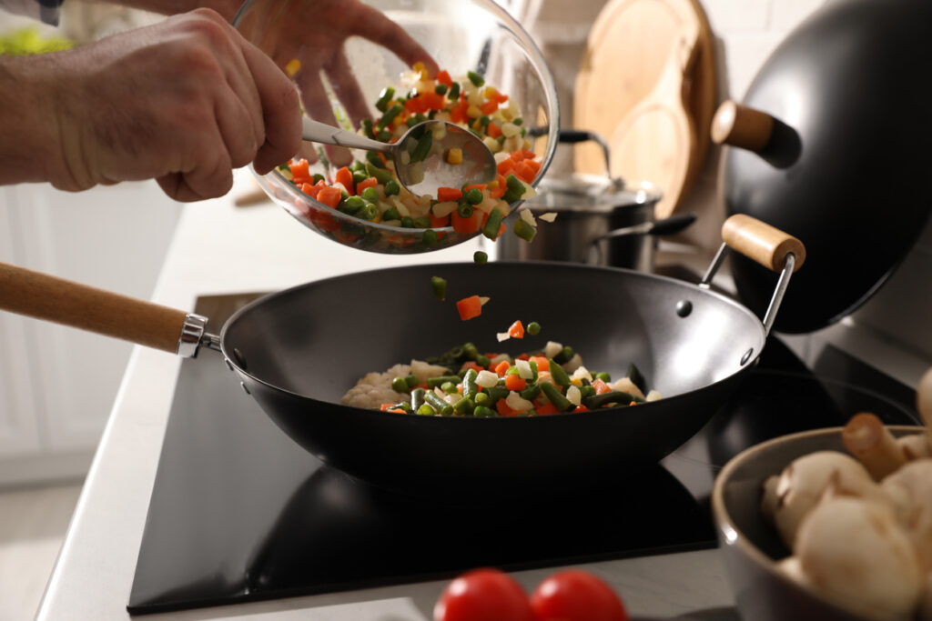 Man pouring mix of fresh vegetables into frying pan, closeup.