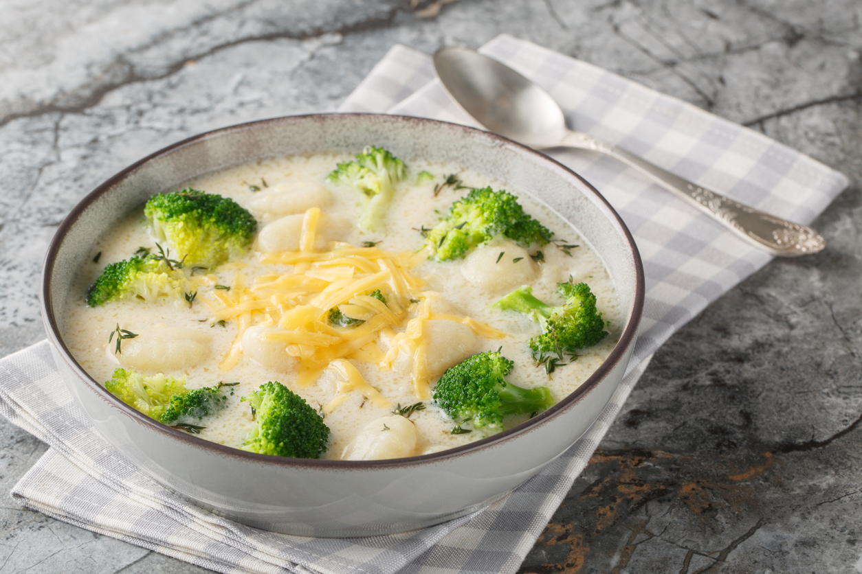 Spicy creamy broccoli gnocchi soup with cheddar cheese, thyme, onion and garlic close-up in a plate on the table.