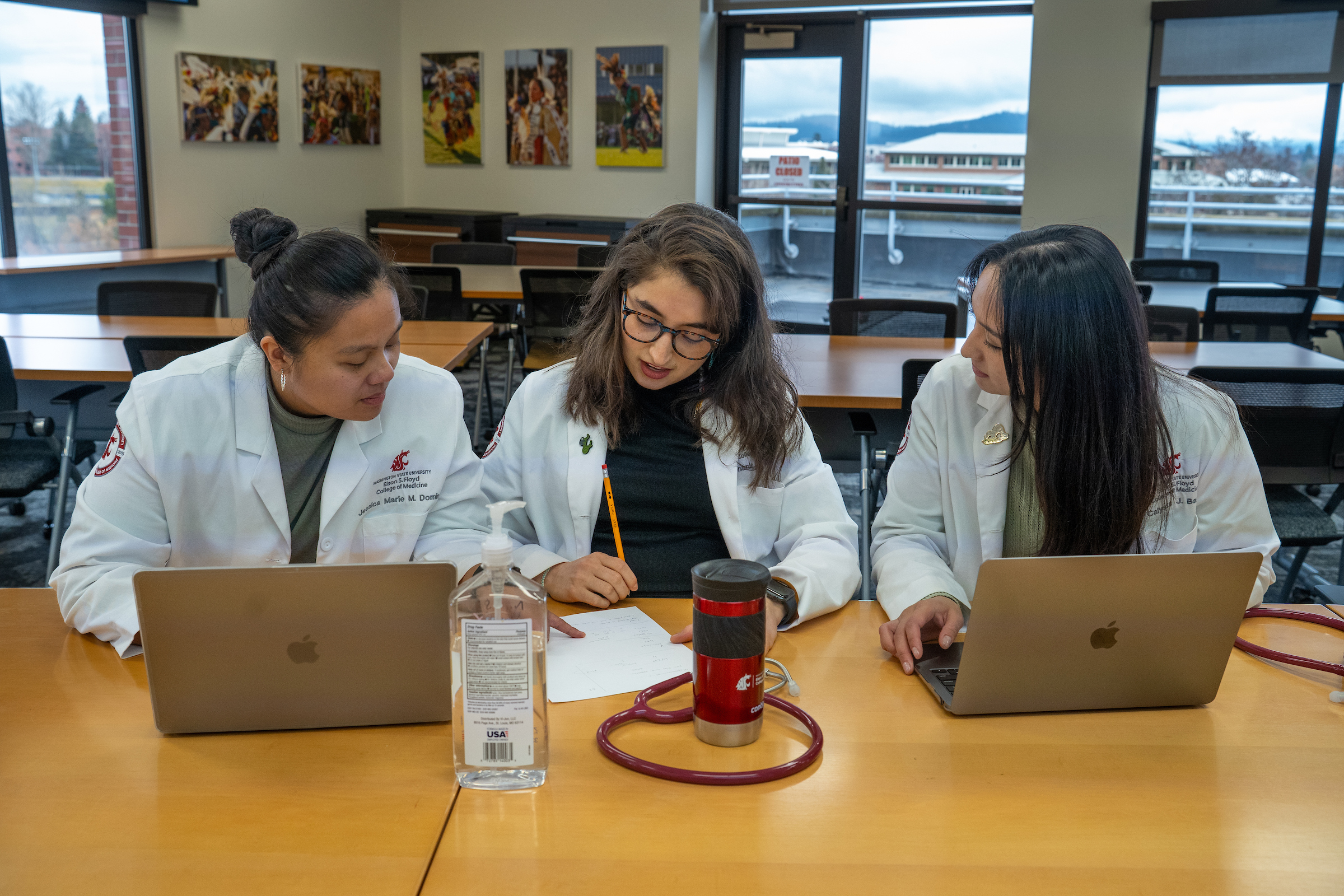 Three students working on tasks facing each other at a desk