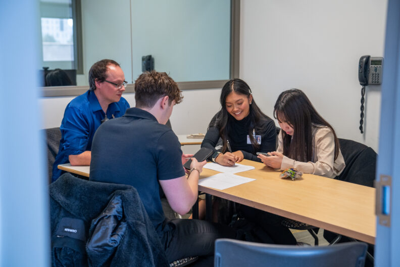 A photo of Doctor of Pharmacy students including Victoria Nuon in a pharmacy communications lab. Students are working in a group working together in writing notes.