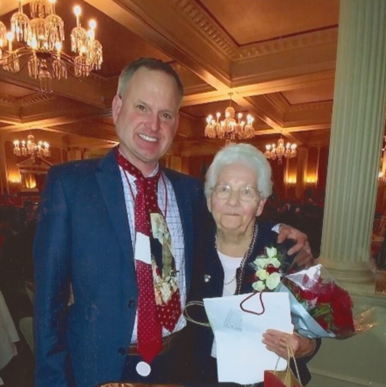 Ian Warren is standing to the left his mother Janet Ruth Warren who is holding a bouquet of red roses.