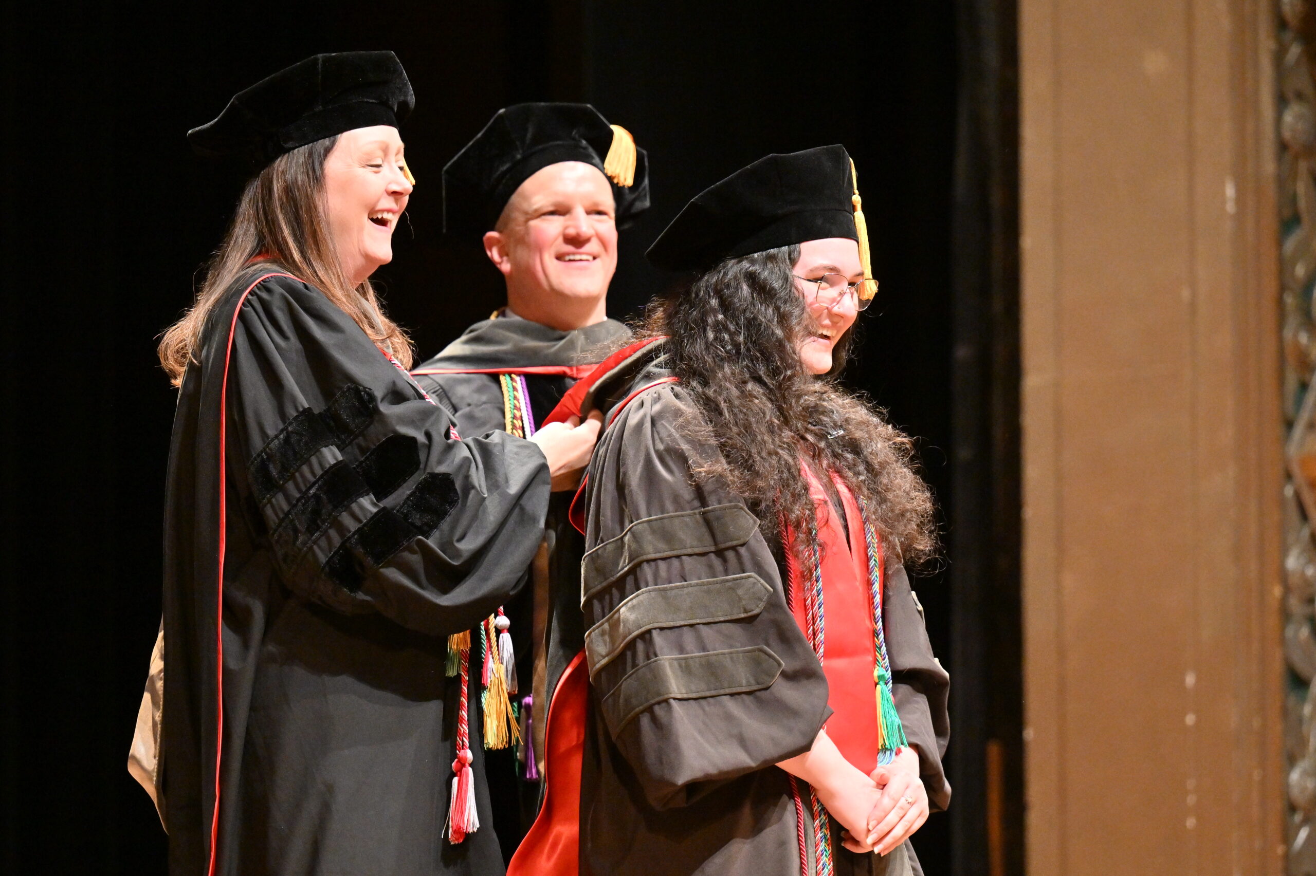 Doctor of Pharmacy graduate smiles while being hooded by faculty on stage