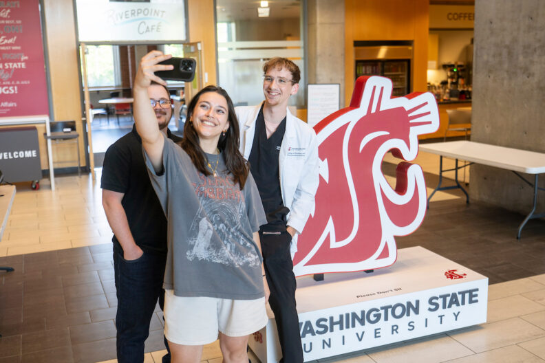 Three students taking a selfie with the Coug head display.