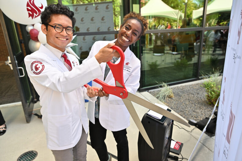 MD students in white coats holding giant scissors 