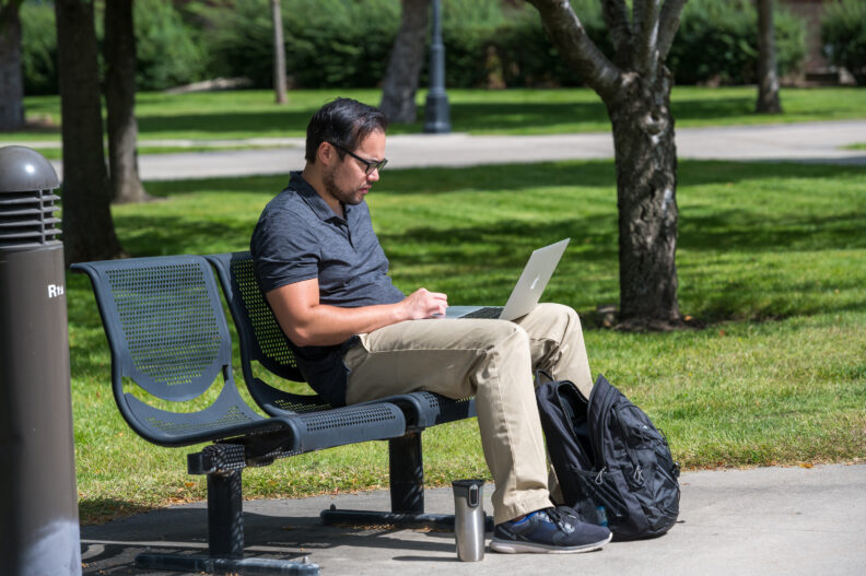person sitting outside on bench with laptop and green grass behind them