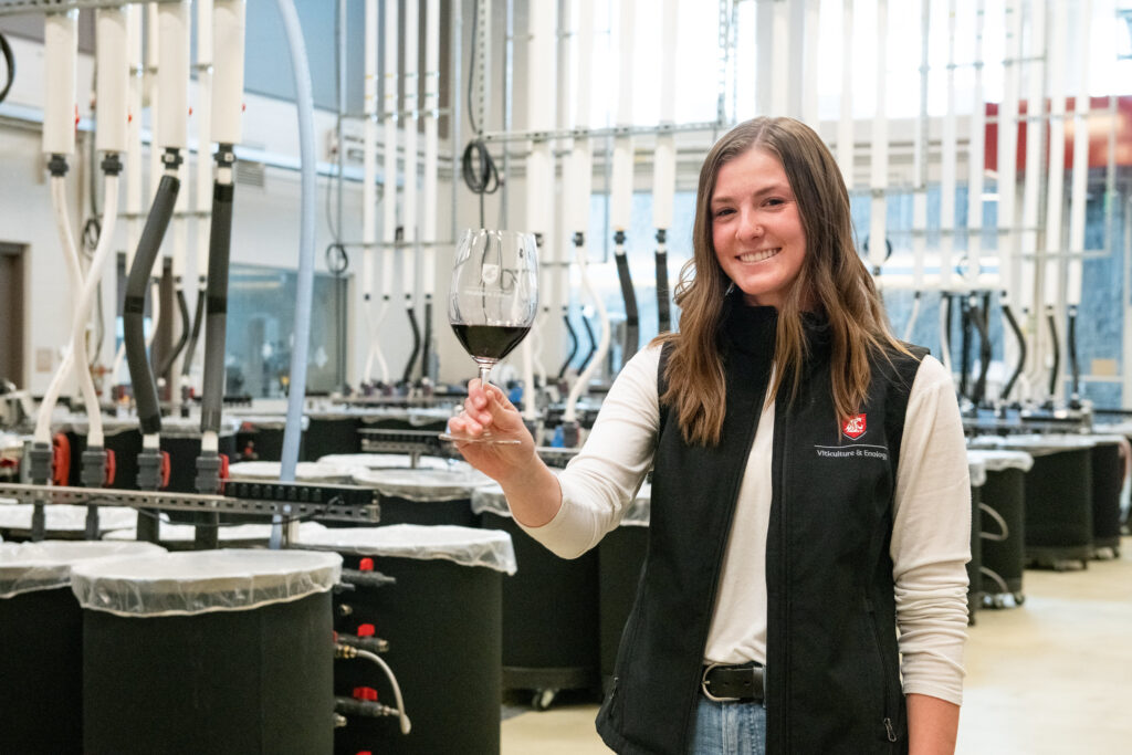 Girl in the WSU Wine Science Center holding a WSU-branded wine glass filled with red wine.