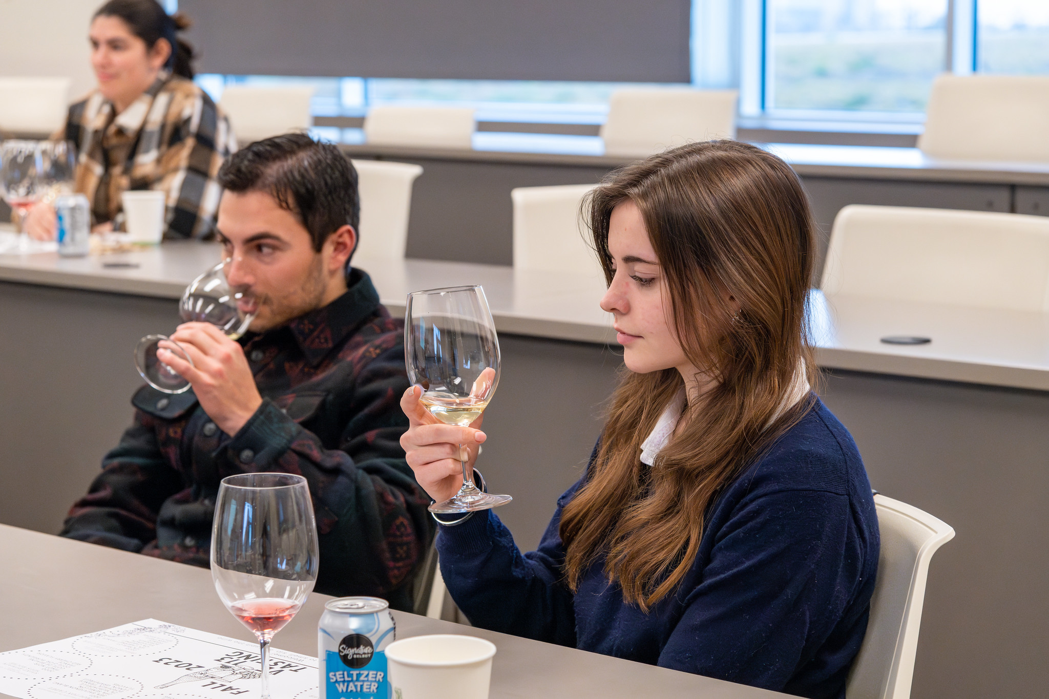 Three students participating in a wine tasting in a classroom.