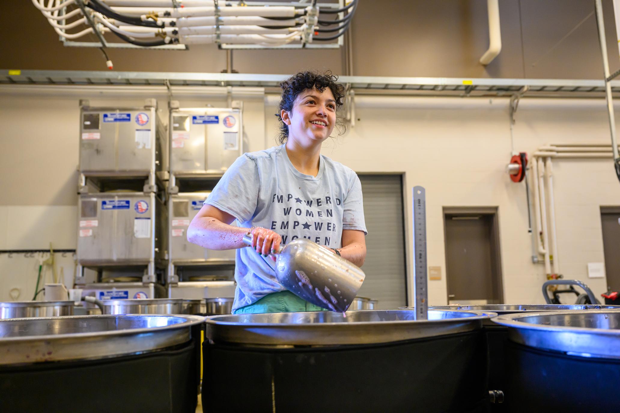 Student scooping wine grapes into large metal barrels.