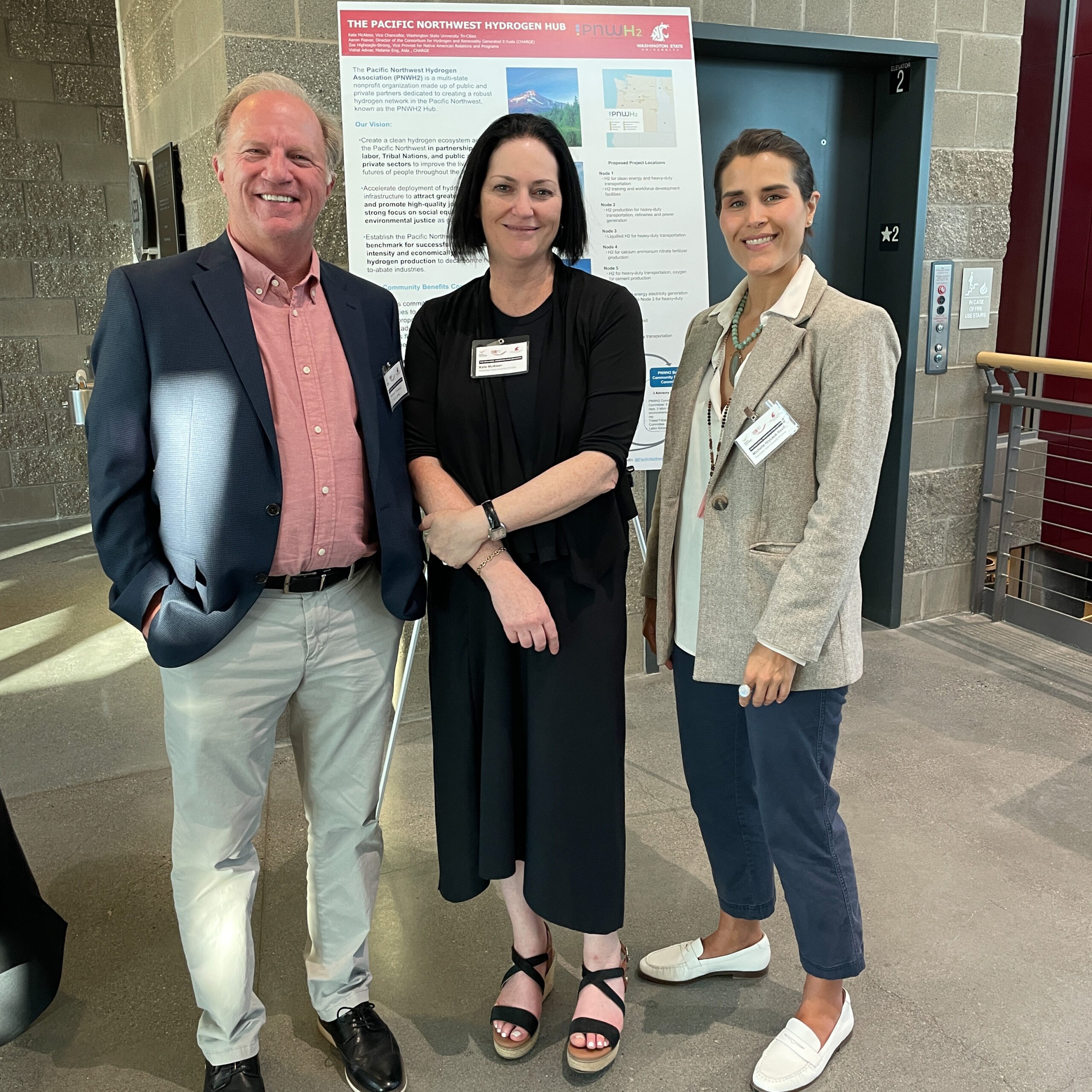 Bob Bauman, Kate McAteer, and Michelle stand in front of a poster.  