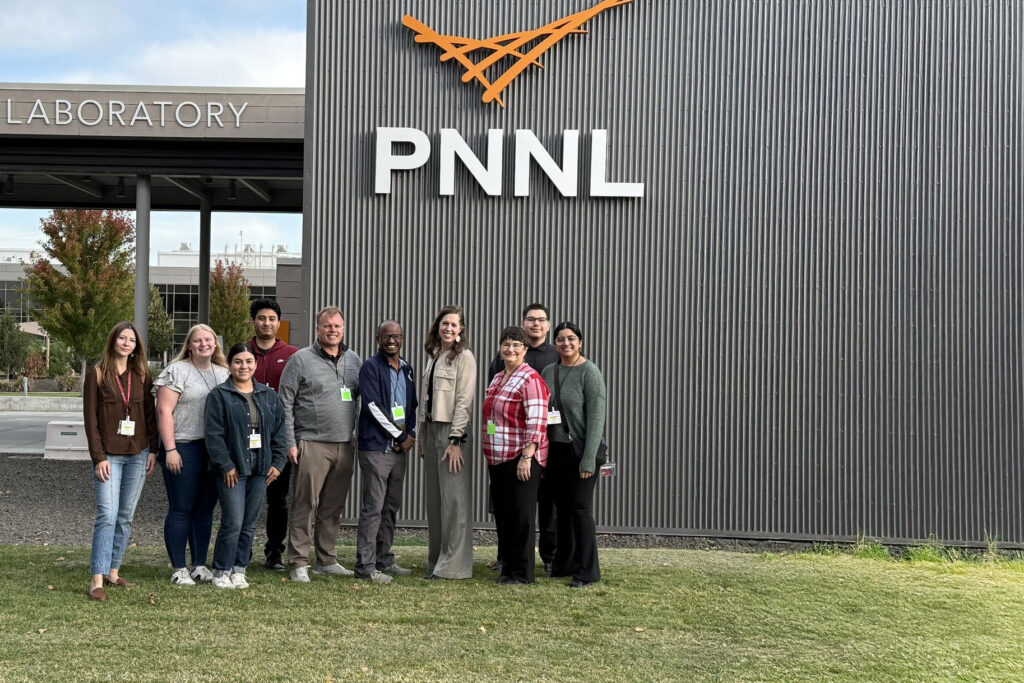 Students seated around a table with laptops talking to each other.