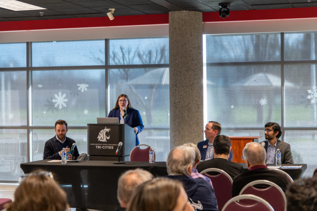 Guest speakers at a table in front of a seated audience.