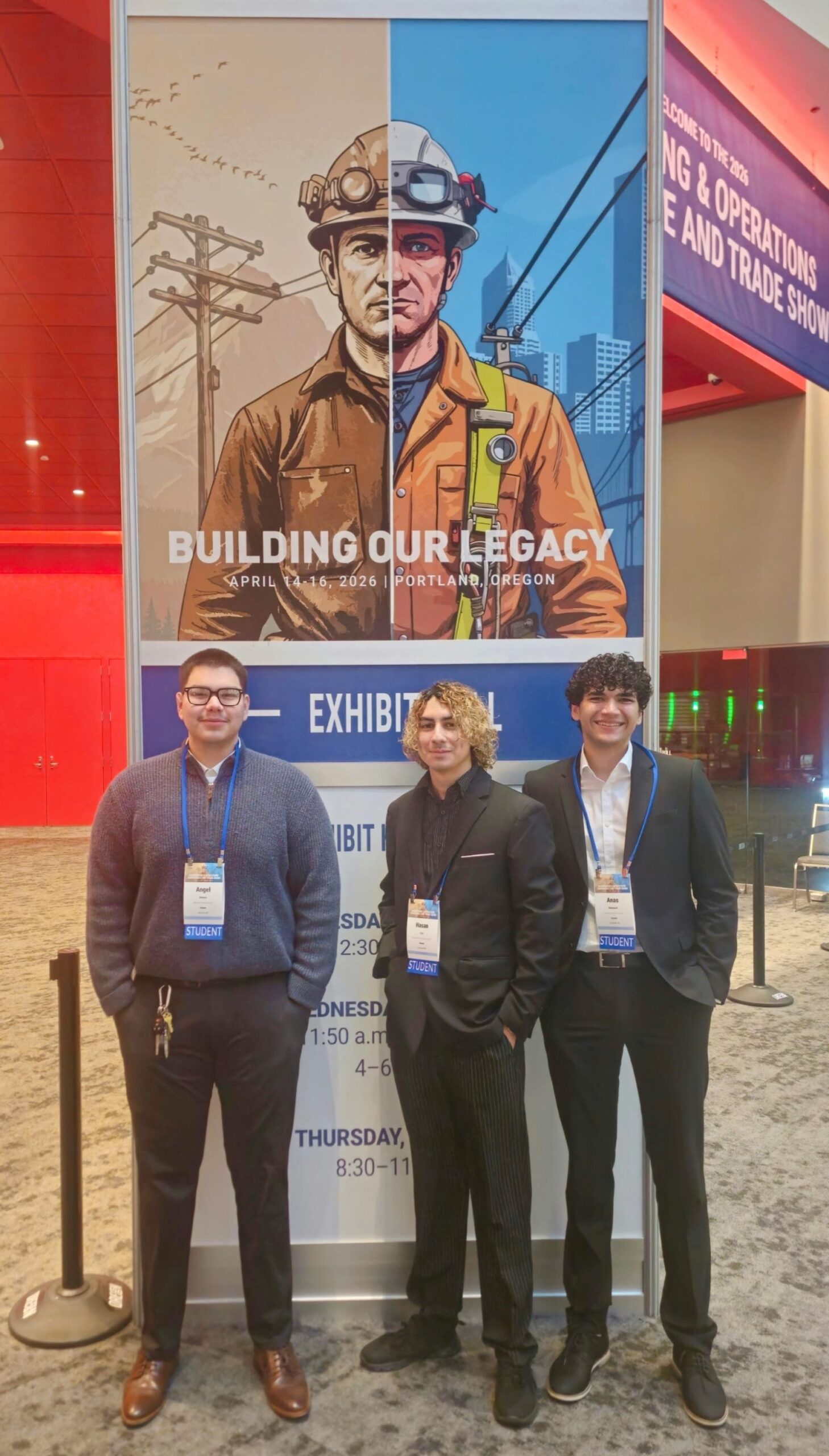 Three men stand in front of conference sign showing an illustrated utility worker.