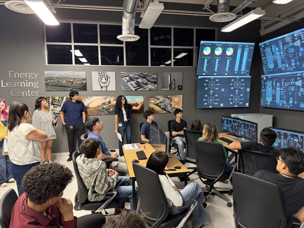 High school and college students stand and sit in office chairs while looking at large TV monitors in a room with signage that reads "Energy Learning Center"