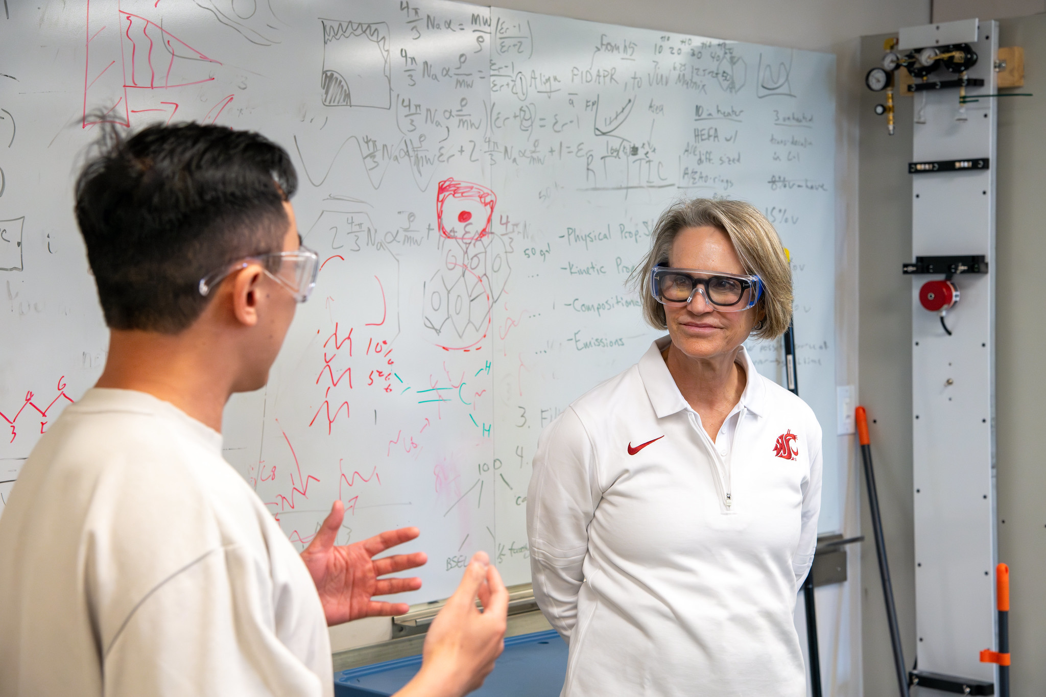 WSU President Elizabeth Cantwell listening to SOAR lab member speak in front of a whiteboard covered in notes and equations.