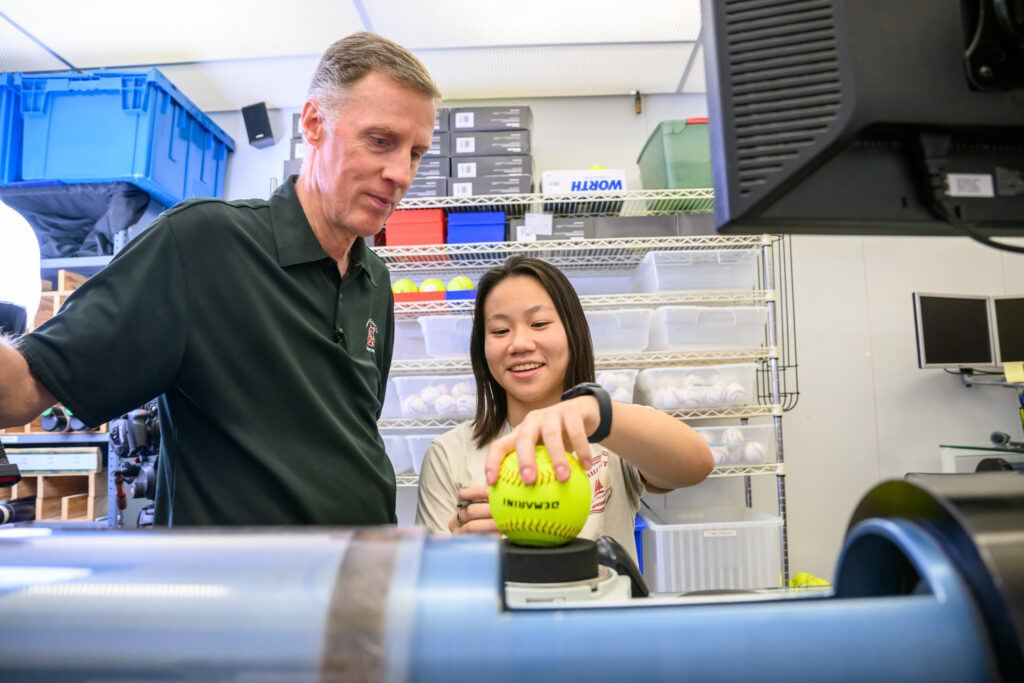 Two people testing a softball on measuring equipment.